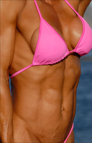 Female bodybuilder Joanna Thomas flexes her muscles while doffing a pink dress